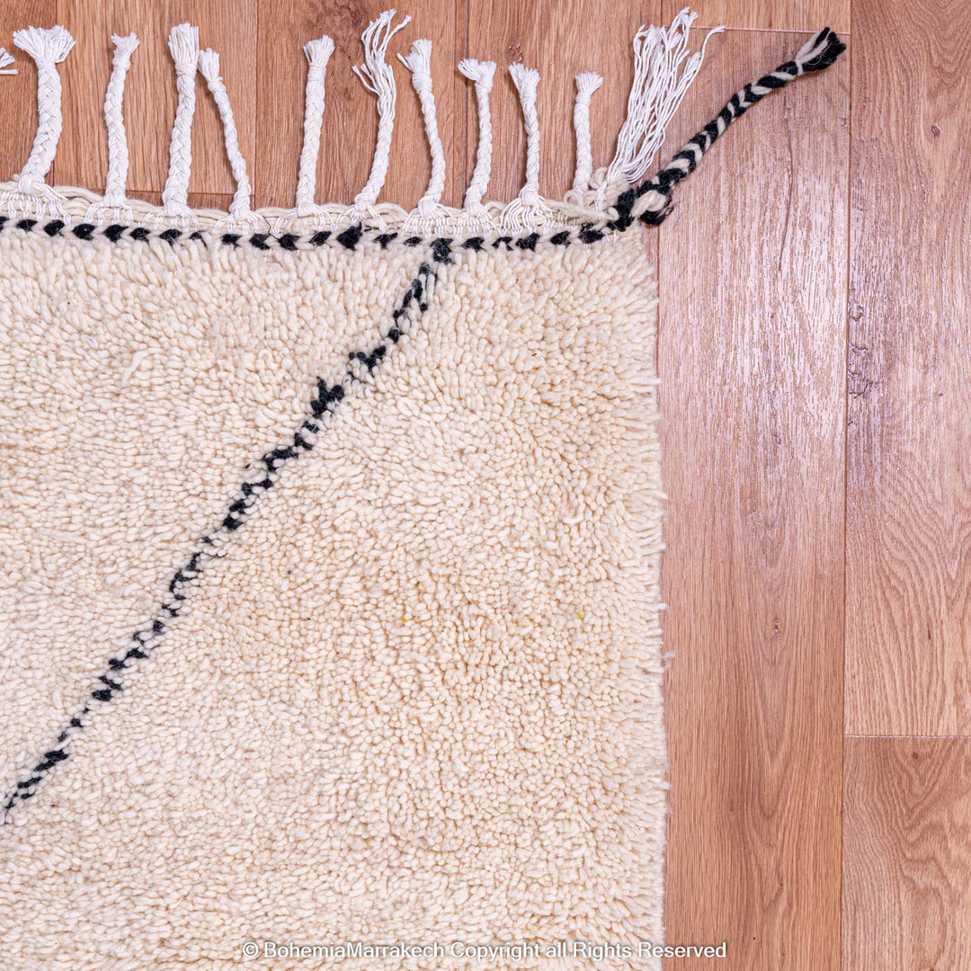 Handmade black and white Moroccan wool rug with diamond pattern, showcasing tassels on a wooden floor, perfect for elegance.