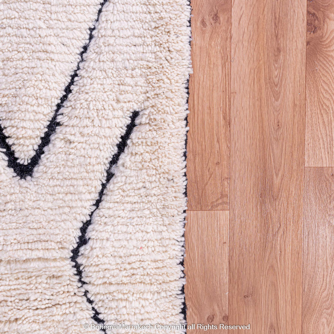 Close-up of a handmade wool Moroccan rug with black diamond pattern on a wooden floor.
