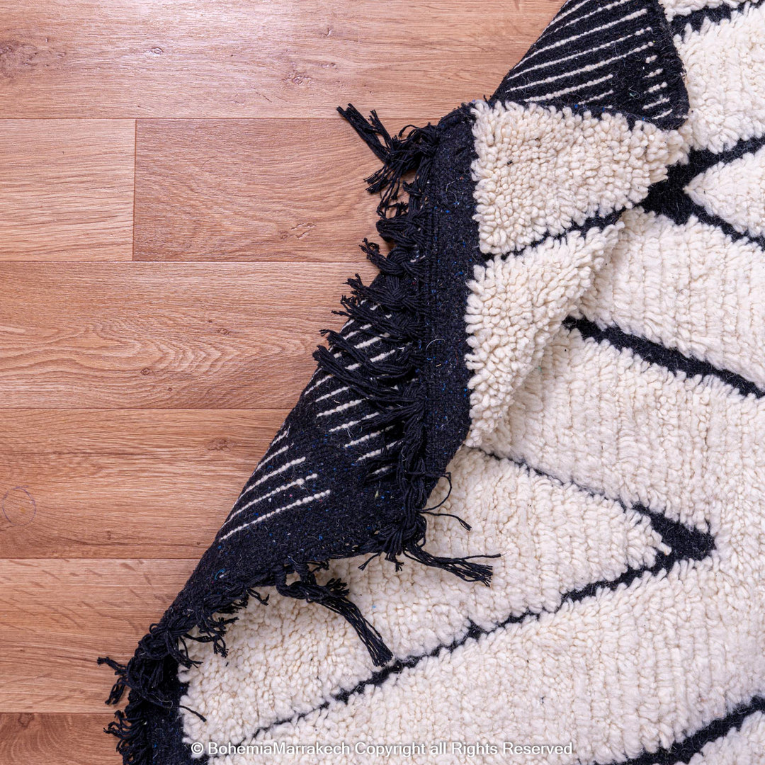 Black and white diamond Moroccan wool rug with traditional Berber design on natural wood floor. Perfect for modern interiors.