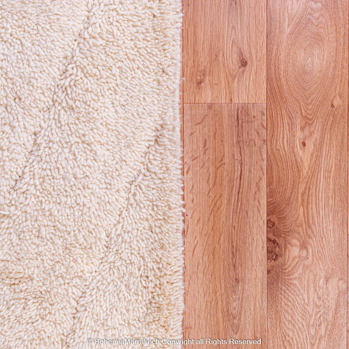 Cream Moroccan wool rug with geometric lines beside wooden floor, showcasing handcrafted elegance and texture.