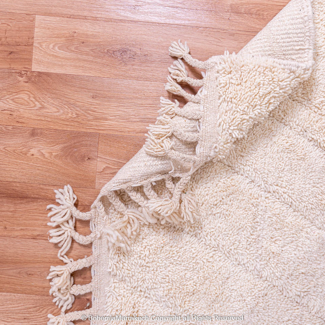 Handmade cream Moroccan Berber rug with geometric patterns on wooden floor
