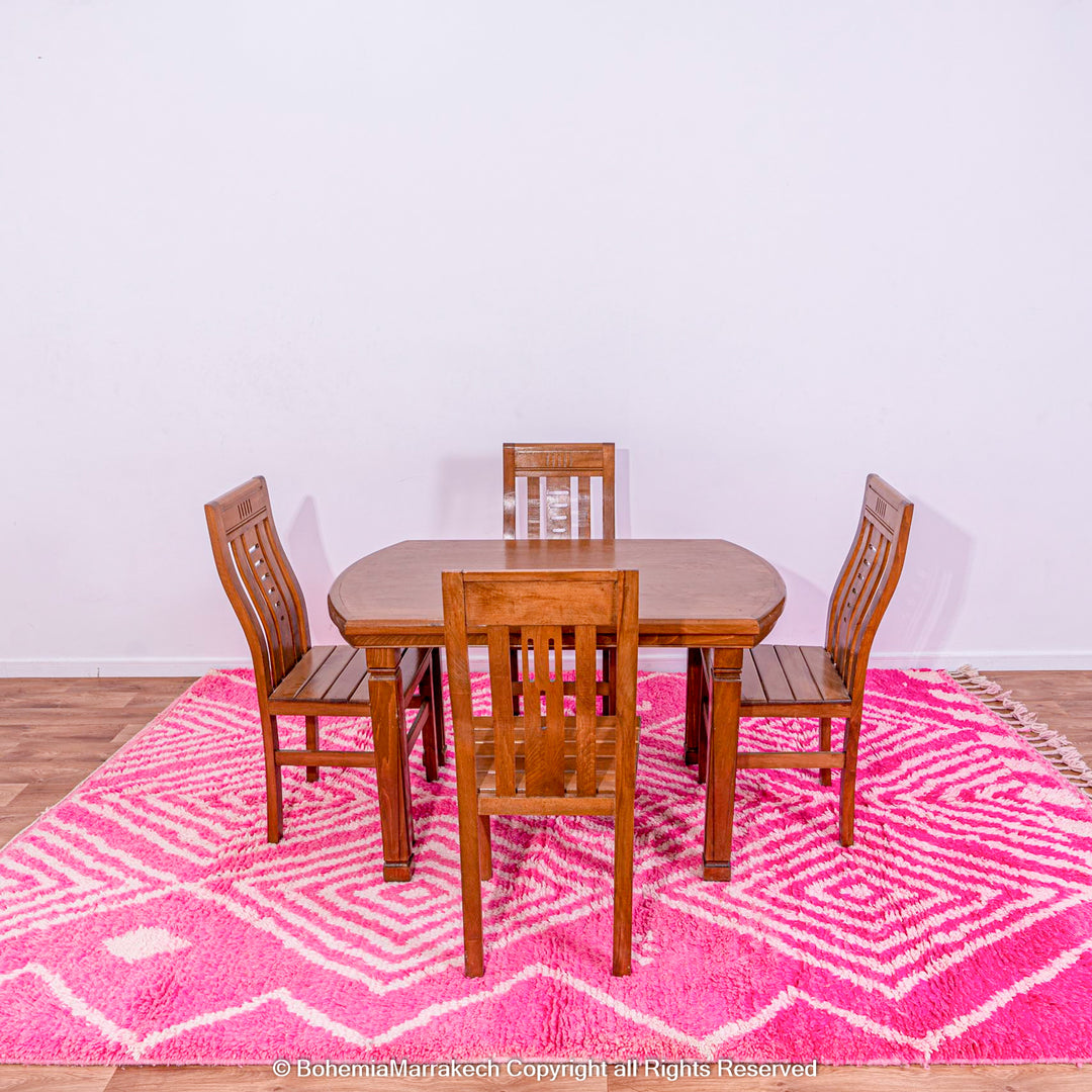 Handmade pink Moroccan rug with white diamond patterns under a wooden dining table set, showcasing Berber weaving tradition.