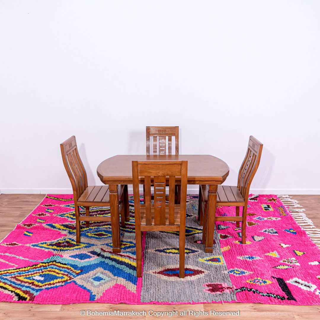 Pink Moroccan rug with colorful Berber motifs under dining set, showcasing vibrant Moroccan artistry.