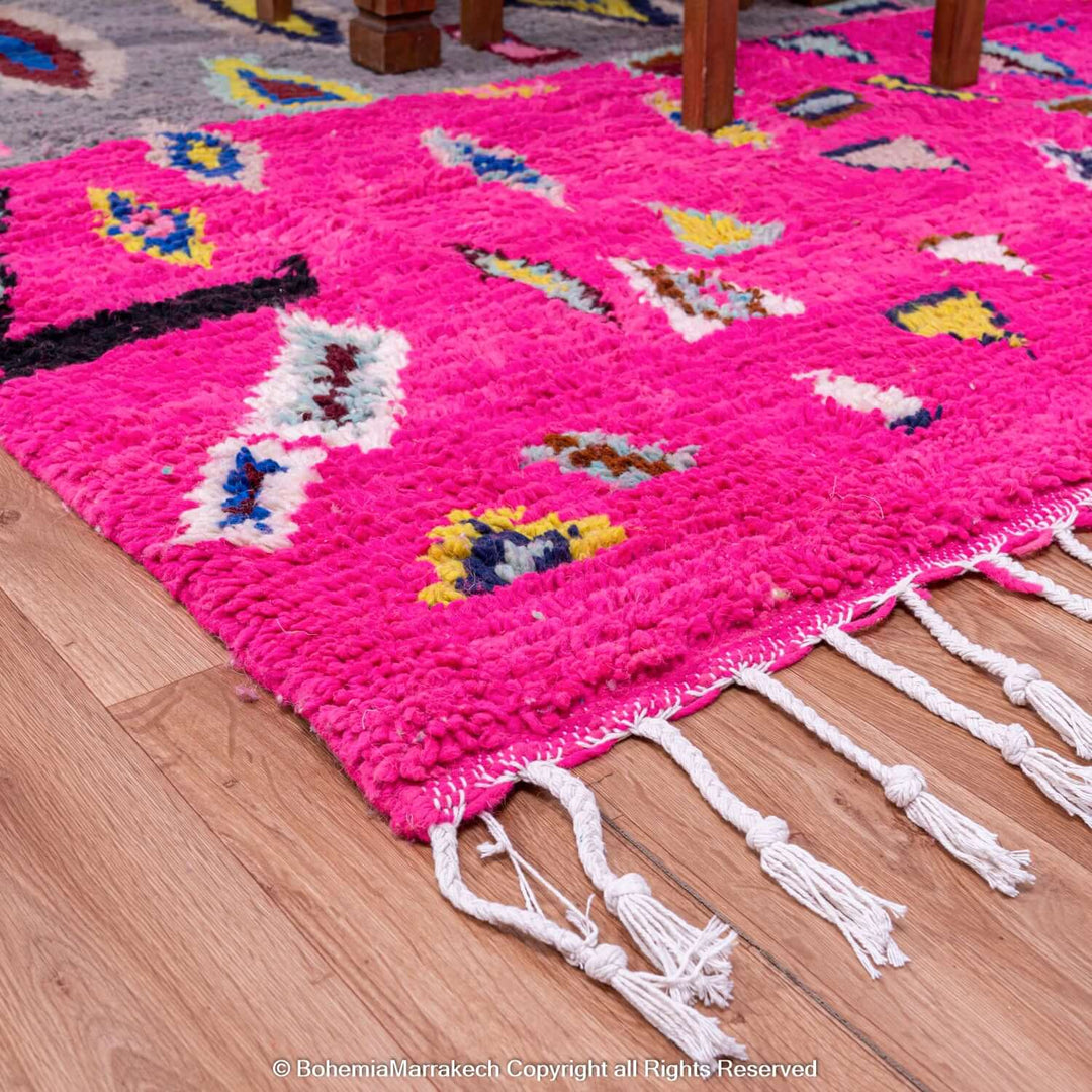 Vibrant pink Moroccan Berber rug with multicolored motifs, showcasing traditional craftsmanship in a modern style, on hardwood floor.