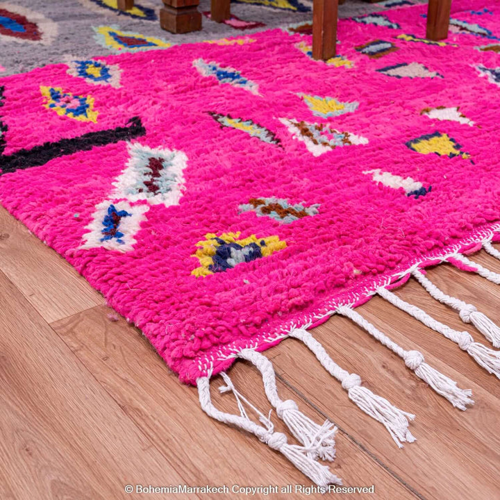 Vibrant pink Moroccan Berber rug with multicolored motifs, showcasing traditional craftsmanship in a modern style, on hardwood floor.