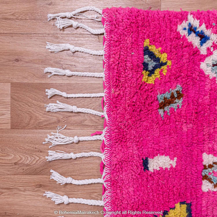 Bright pink Moroccan Berber rug with multicolor motifs, showcasing traditional craftsmanship on wooden floor.