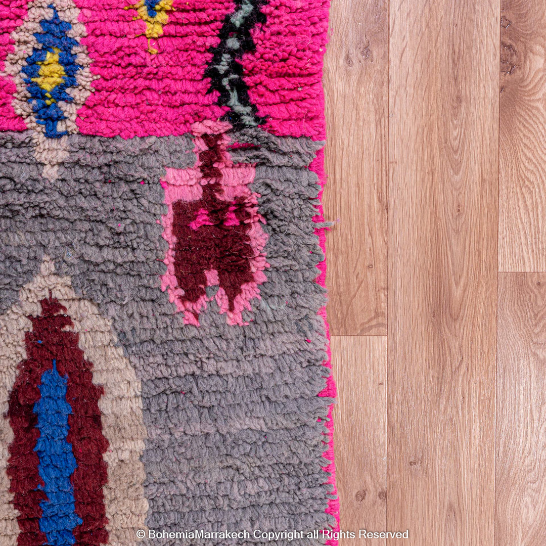 Close-up of a vibrant pink Moroccan Berber rug with traditional motifs on a wooden floor, featuring colors like gray, blue, and red.