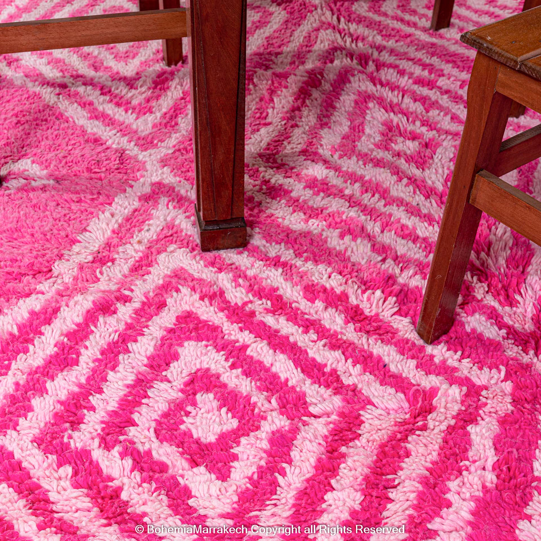 Pink Moroccan rug with white diamond patterns under wooden furniture, handmade Berber wool.