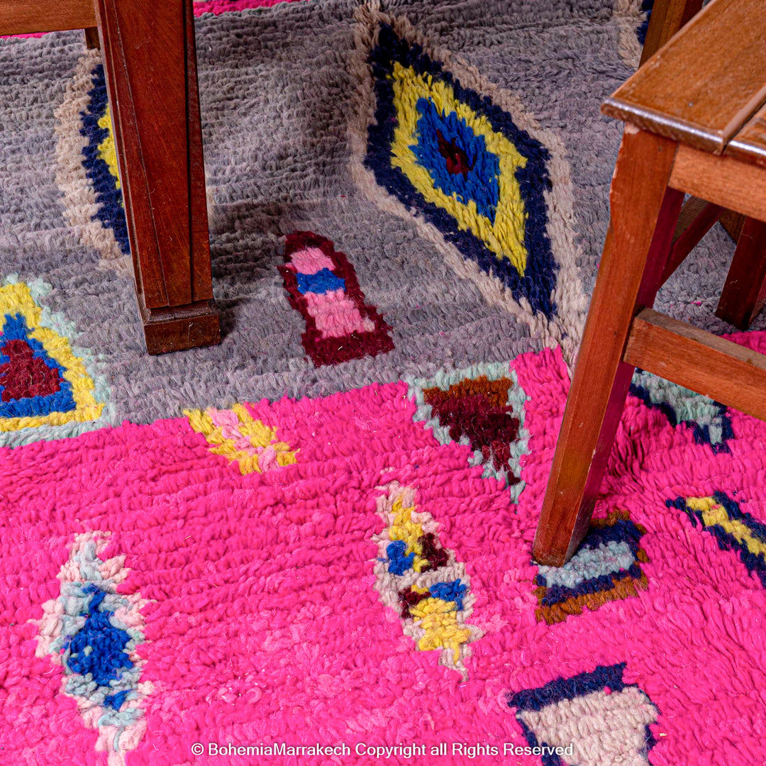 Bold pink Moroccan rug with colorful Berber motifs, handmade from natural wool, complements wooden furniture. Moroccan rug, home decor.