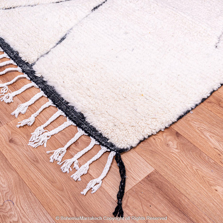 White Moroccan Beni Ourain wool rug with black lines and fringes, ideal for modern interiors.