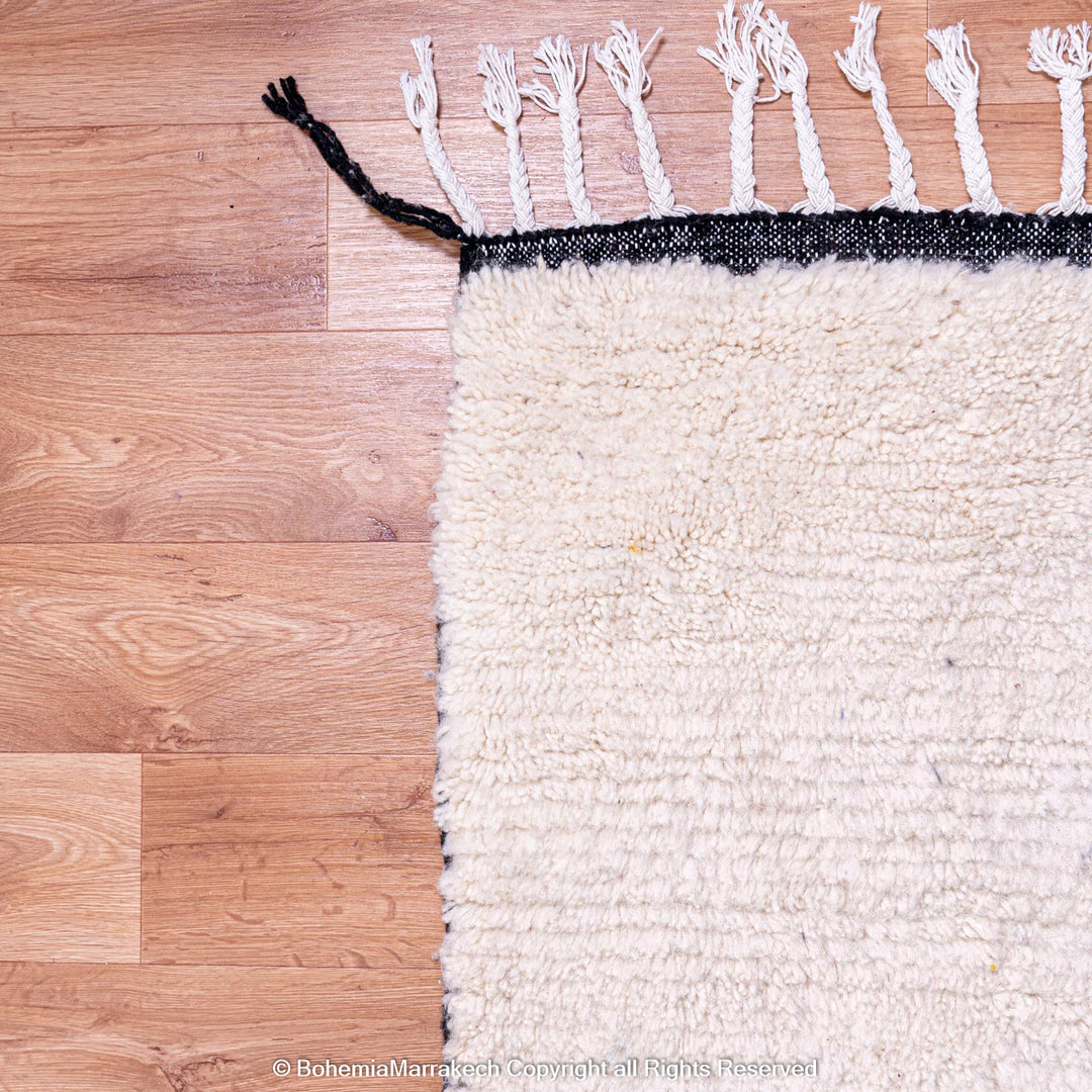 White Moroccan rug with black lines, wool Beni Ourain style on wooden floor.