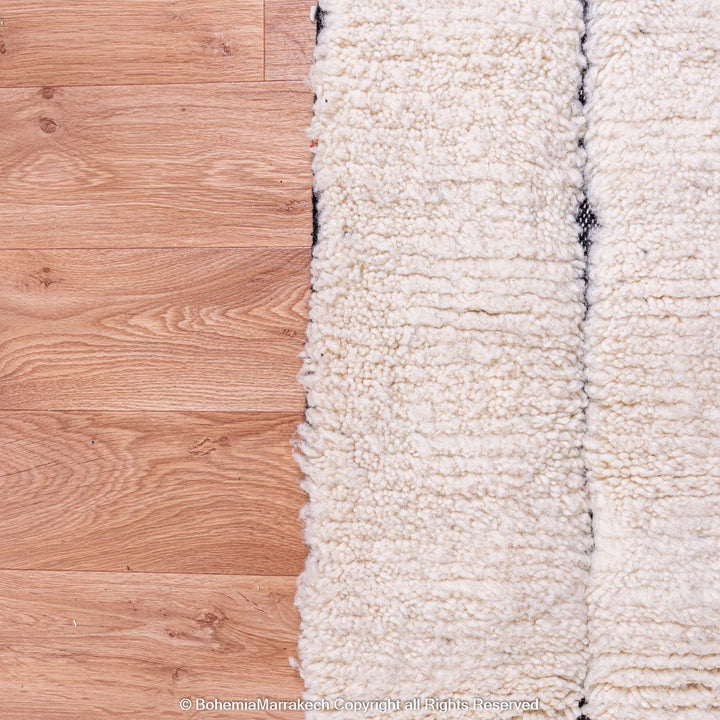 White Moroccan Beni Ourain rug with black lines on wooden floor, showcasing wool texture and traditional design.