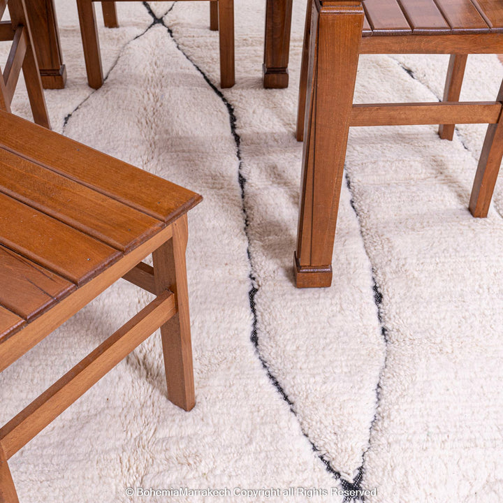 White Moroccan rug with black lines under wooden chairs, traditional Beni Ourain wool design, ideal for modern and boho interiors.
