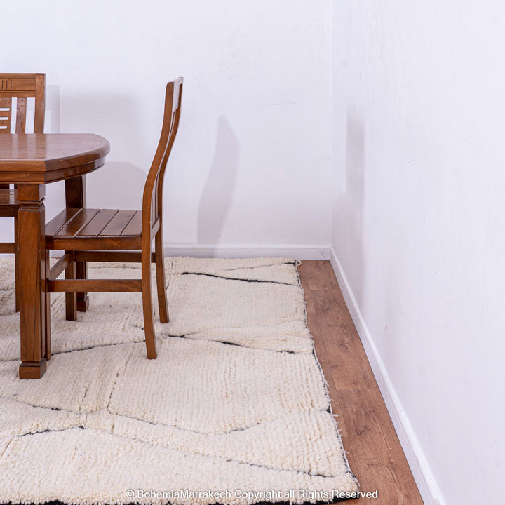 White Moroccan rug with black lines under a wooden dining table in a minimalist room showcasing Beni Ourain wool craftsmanship.