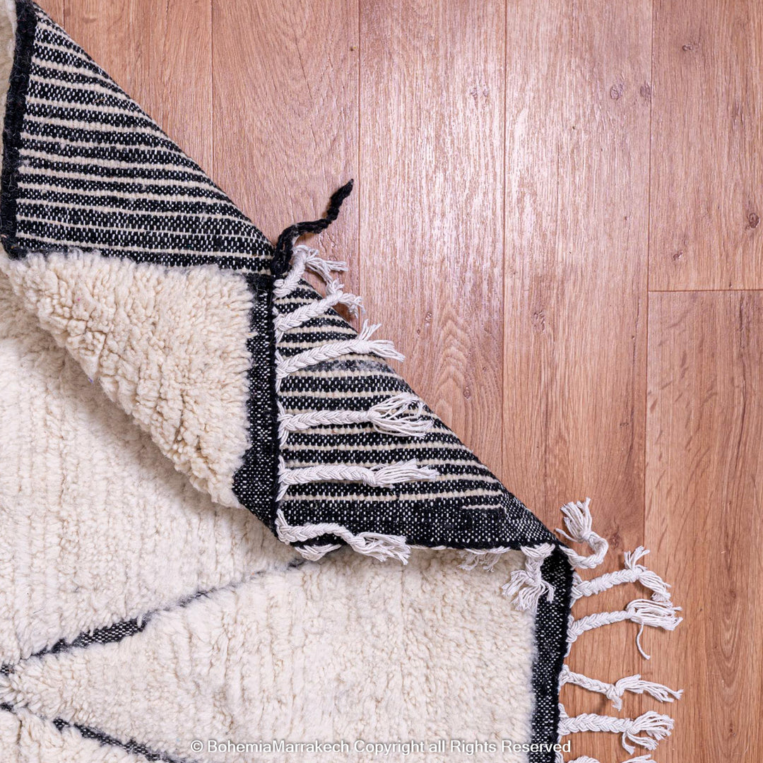 White Moroccan rug with black lines, Beni Ourain style, wool material, displayed on wooden floor.