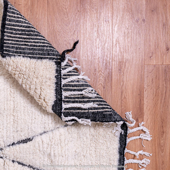 White Moroccan rug with black lines, Beni Ourain style, wool material, displayed on wooden floor.