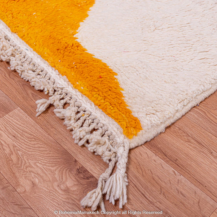 Yellow and cream Moroccan wool rug with tassels on wooden floor, showcasing abstract design. Modern Moroccan Berber carpet, 8x10.