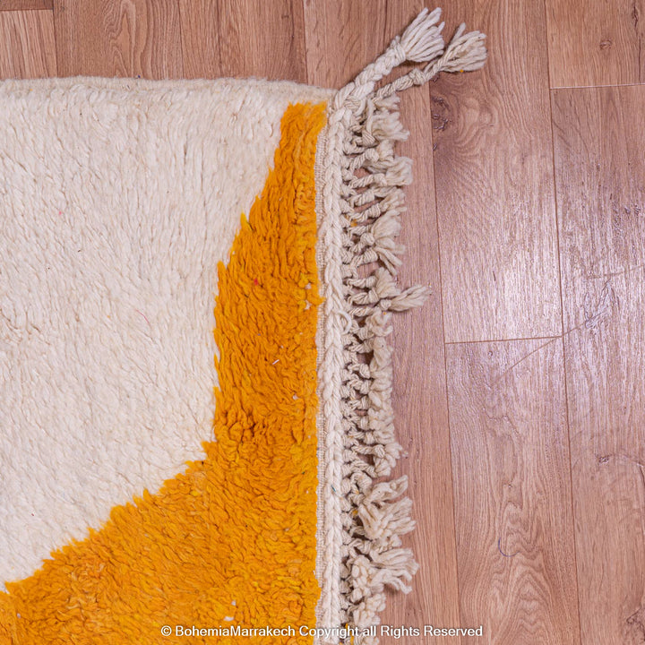 Corner of modern Moroccan wool rug with yellow and navy abstract design on wooden floor.