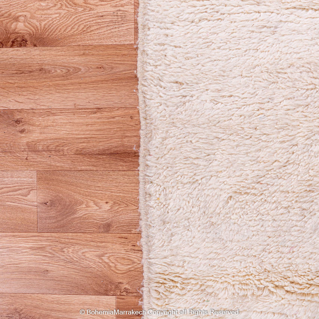Close-up of cream ivory Moroccan wool rug on hardwood floor, showcasing soft texture and handmade quality.
