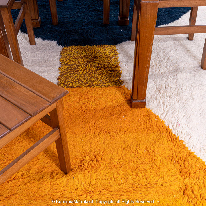 Modern Moroccan wool rug with yellow, navy, and cream abstract design, showcasing a bold and artistic aesthetic under wooden furniture.