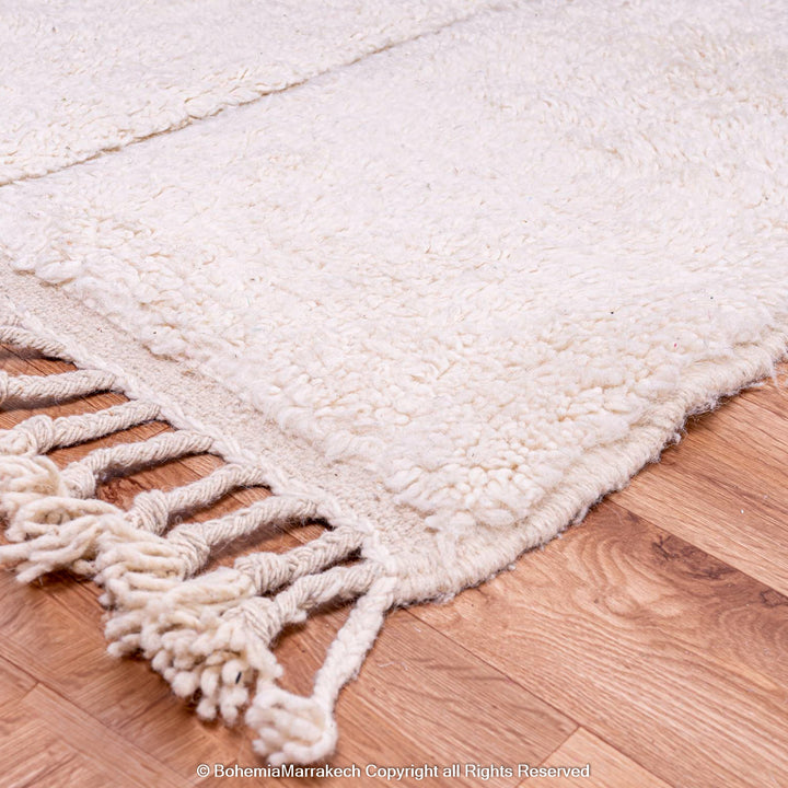 White Moroccan wool rug with fringe on wood floor, featuring a minimalist grid pattern. Perfect for modern, Scandinavian decor.