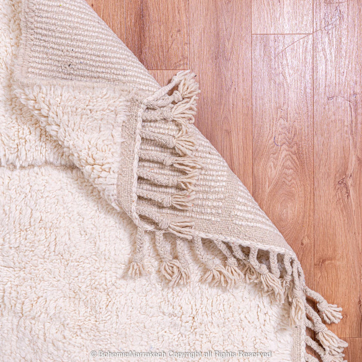 White Moroccan wool rug with a geometric grid pattern on a wooden floor, featuring fringed edges.