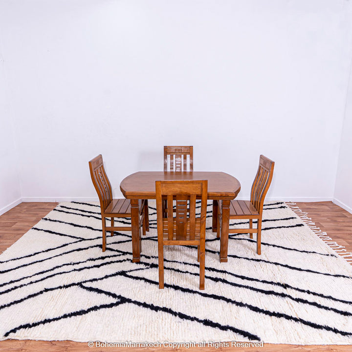 Black and white Beni Ourain Moroccan wool rug with criss-cross patterns under wooden dining table setting.
