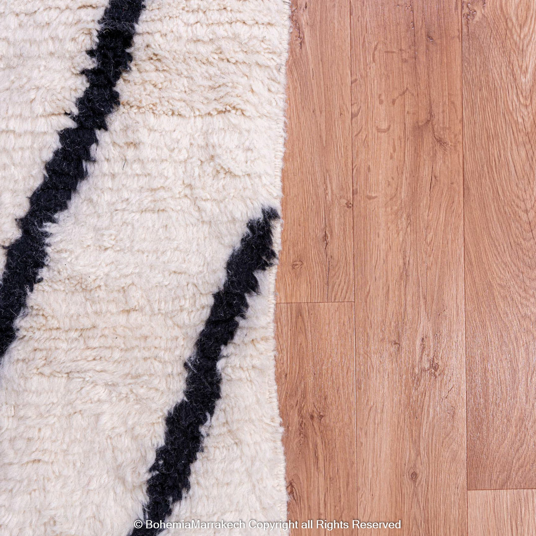 Black and white Moroccan Beni Ourain wool rug on hardwood floor, showcasing abstract patterns. Traditional Moroccan decor.
