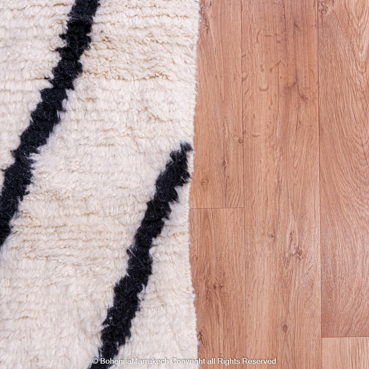 Black and white Moroccan Beni Ourain wool rug on hardwood floor, showcasing abstract patterns. Traditional Moroccan decor.