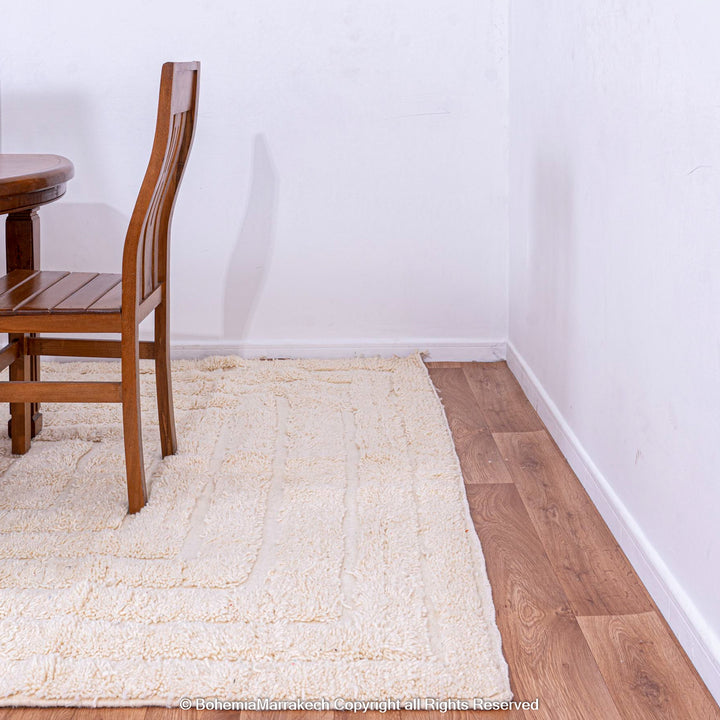 White Moroccan rug with subtle V line texture under wooden dining set on hardwood floor.