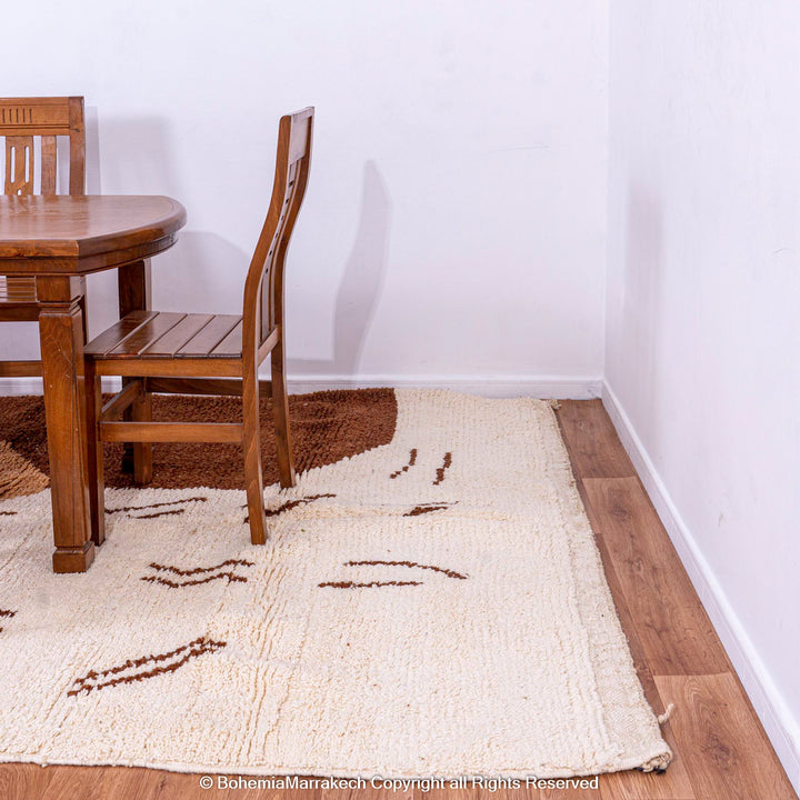 Modern Moroccan rug with abstract brown and beige design placed under dining table.