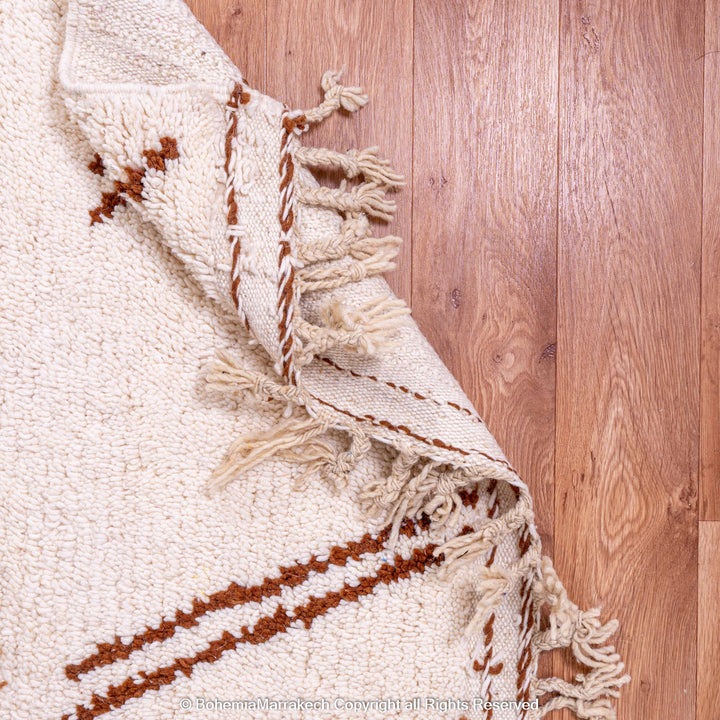 Modern Moroccan wool rug in brown, beige, and white tones, showcasing abstract design on hardwood floor. Ideal for contemporary decor.