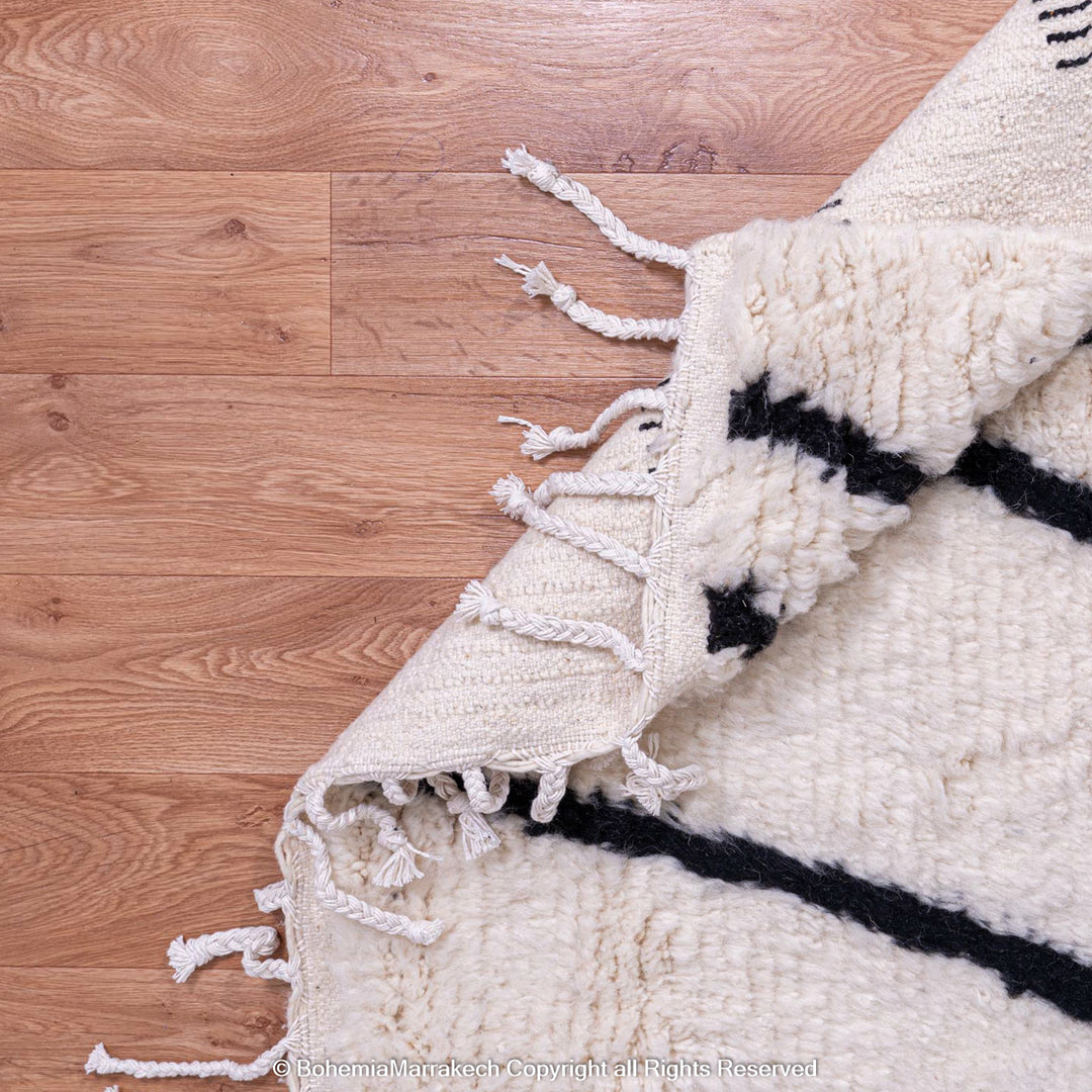Beni Ourain Moroccan wool rug in black and white criss-cross pattern on wooden floor, showcasing minimalist design and craftsmanship.
