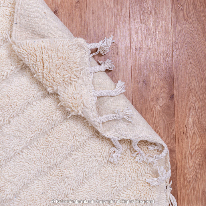 White Moroccan wool rug with subtle V-line texture on wooden floor.