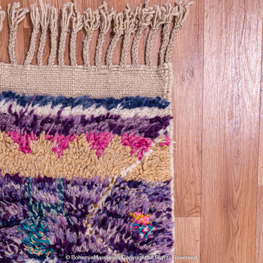 Colorful Moroccan wool rug with fringe, featuring purple, pink, and earthy tribal designs, showcasing Berber craftsmanship.
