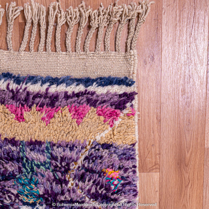 Colorful Moroccan wool rug with fringe, featuring purple, pink, and earthy tribal designs, showcasing Berber craftsmanship.
