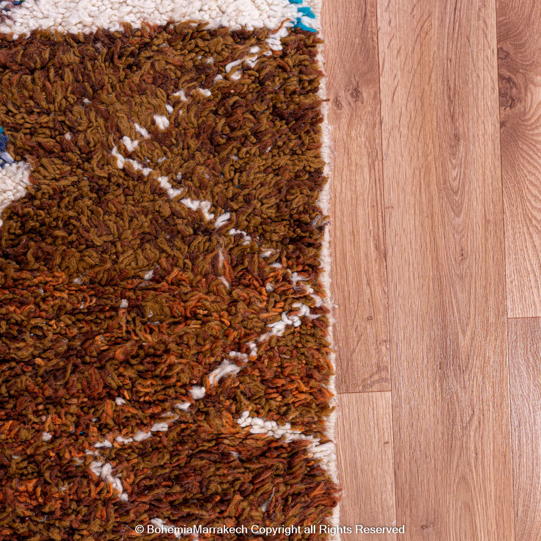 Handmade Moroccan Berber wool rug with tribal motifs in earthy tones on wooden floor.
