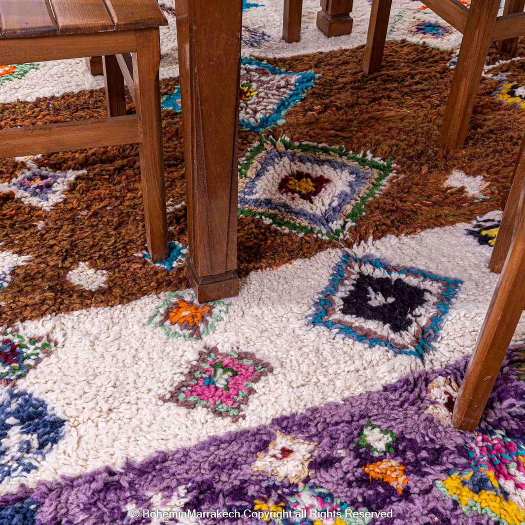Colorful Moroccan wool rug with tribal diamond patterns under a wooden dining table, featuring purple, blue, and brown hues.