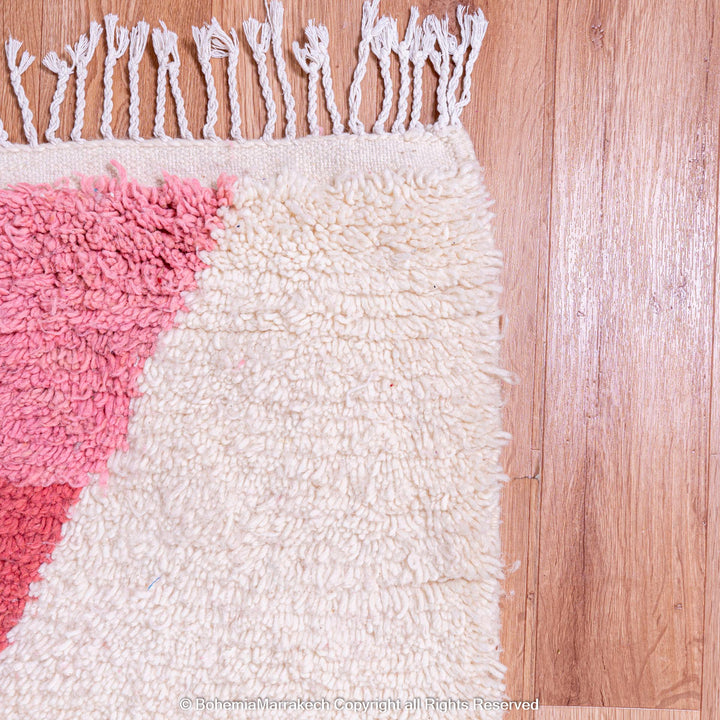 Red and pink Moroccan wool rug corner with tassels on hardwood floor.