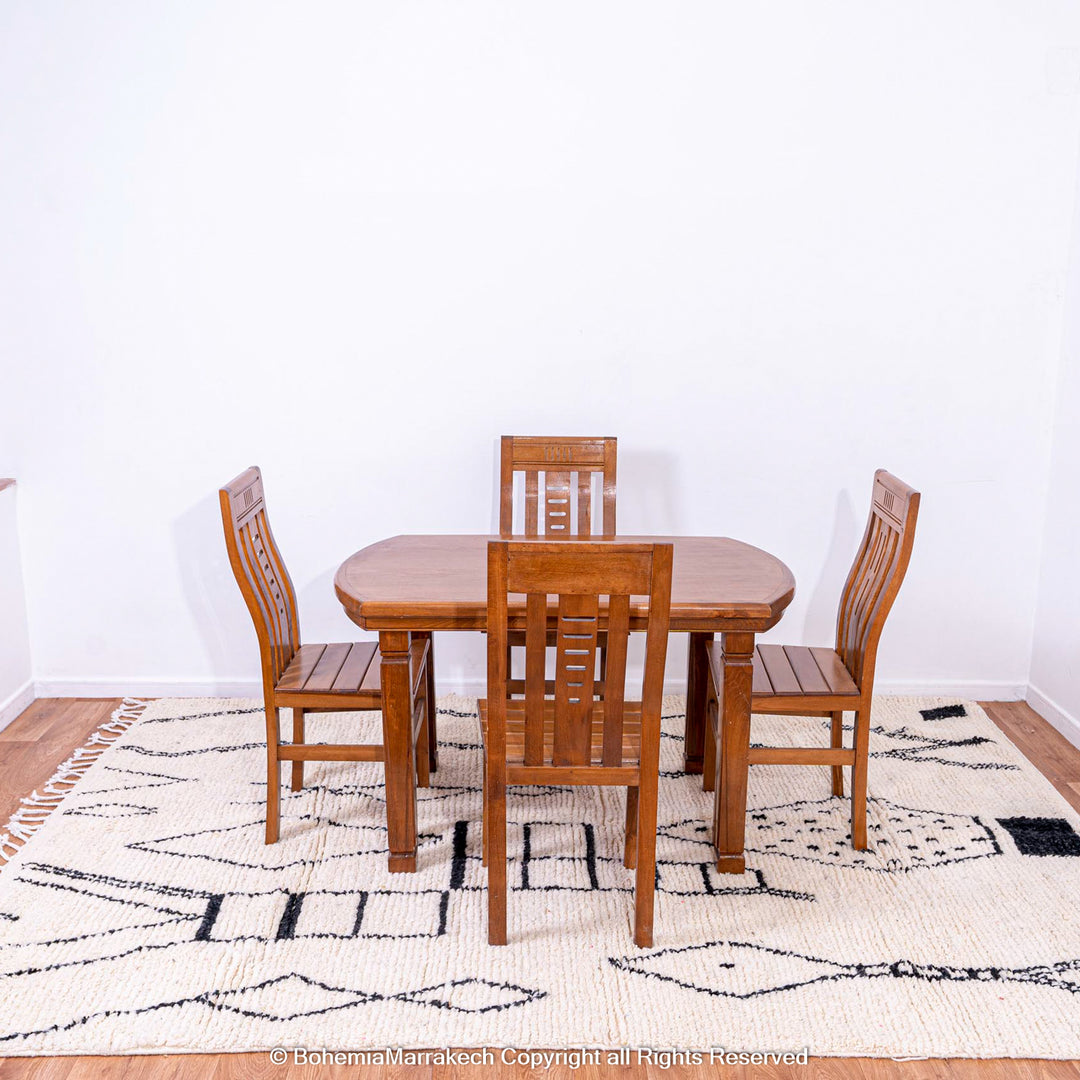 Dining room with wooden table set on white Moroccan rug with black abstract diamond design, handwoven from natural wool.