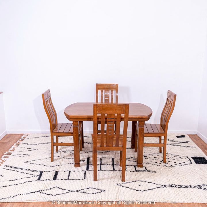 Dining room with wooden table set on white Moroccan rug with black abstract diamond design, handwoven from natural wool.