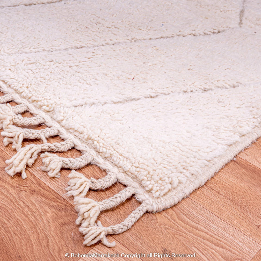 White Moroccan rug with zigzag pattern on wooden floor, showcasing hand-knotted wool texture and tassel details.