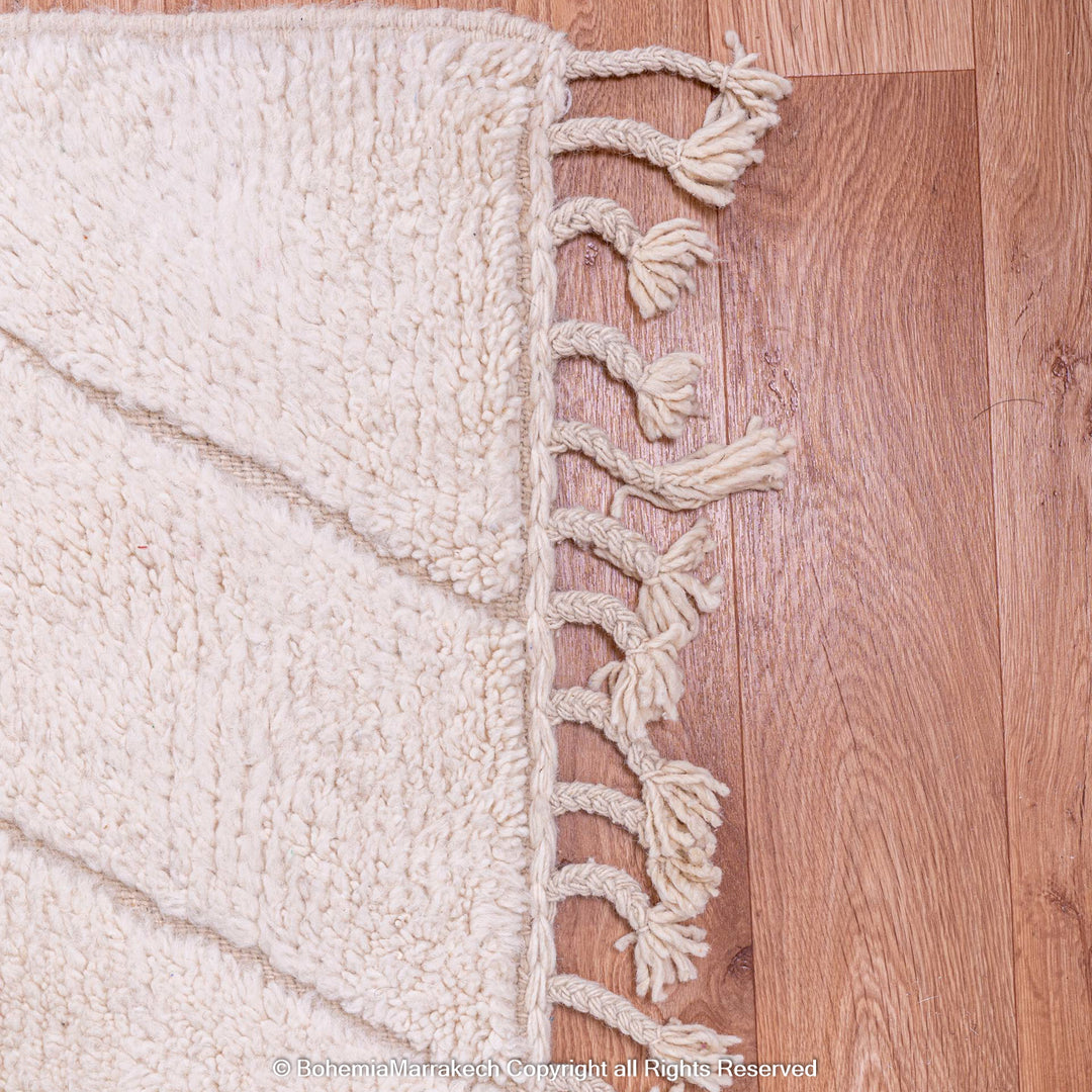 White Moroccan wool rug with zigzag design and fringed edges, showcasing traditional Berber craftsmanship on wooden floor.