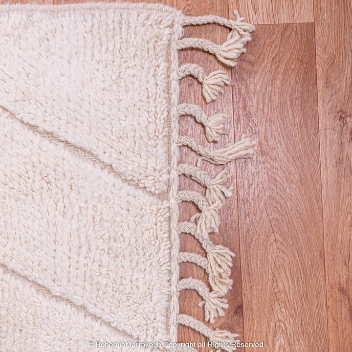 White Moroccan wool rug with zigzag design and fringed edges, showcasing traditional Berber craftsmanship on wooden floor.