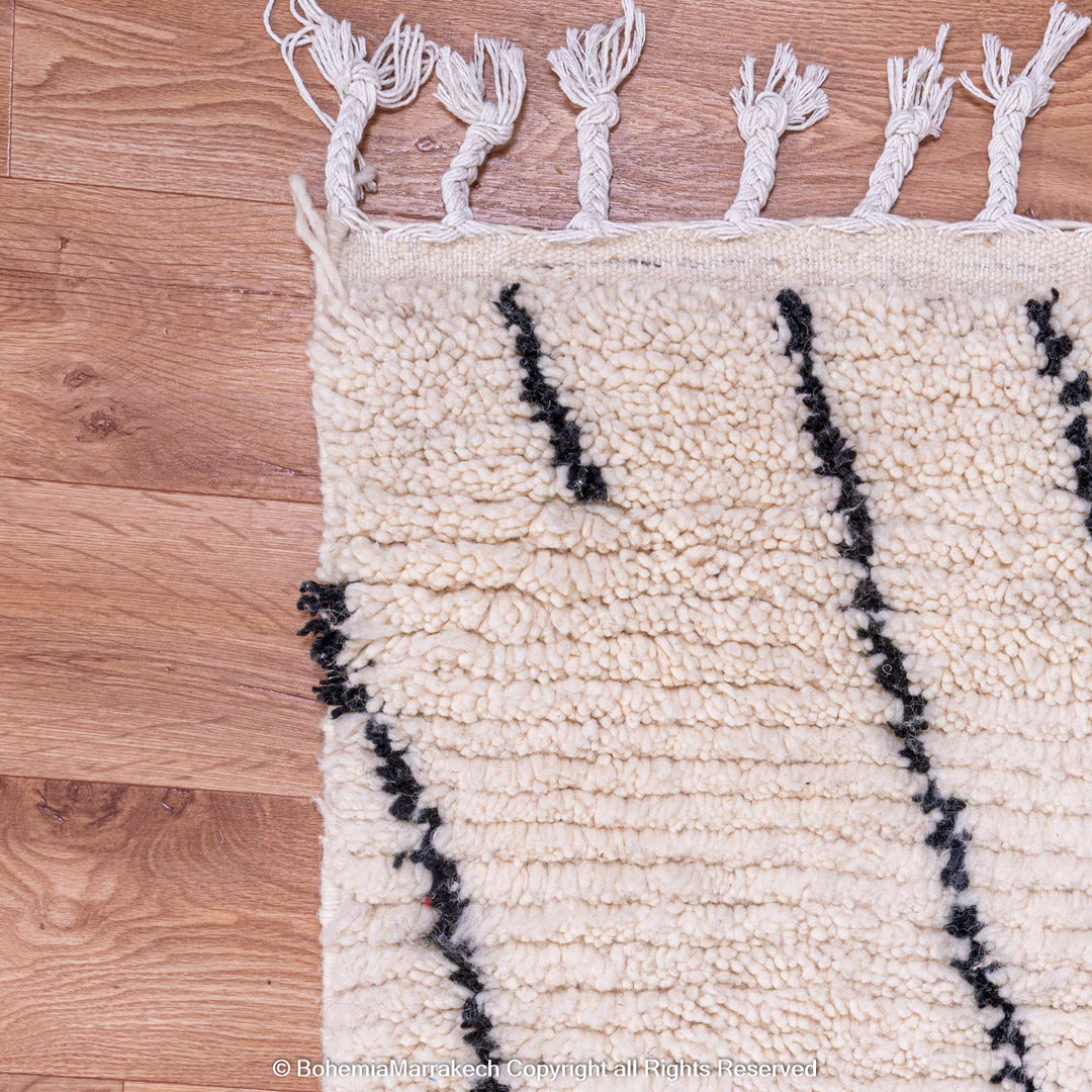 White Moroccan rug with black abstract diamond design on wooden floor, showcasing textured handwoven wool and traditional Berber craftsmanship.