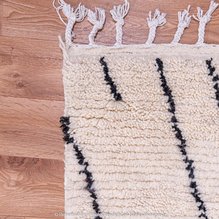White Moroccan rug with black abstract diamond design on wooden floor, showcasing textured handwoven wool and traditional Berber craftsmanship.
