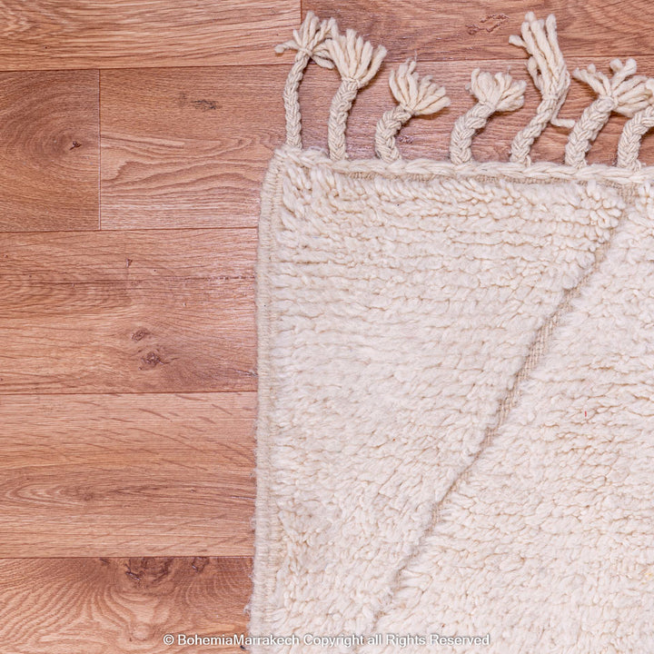 White Moroccan rug corner showing zigzag pattern and tassels on hardwood floor.