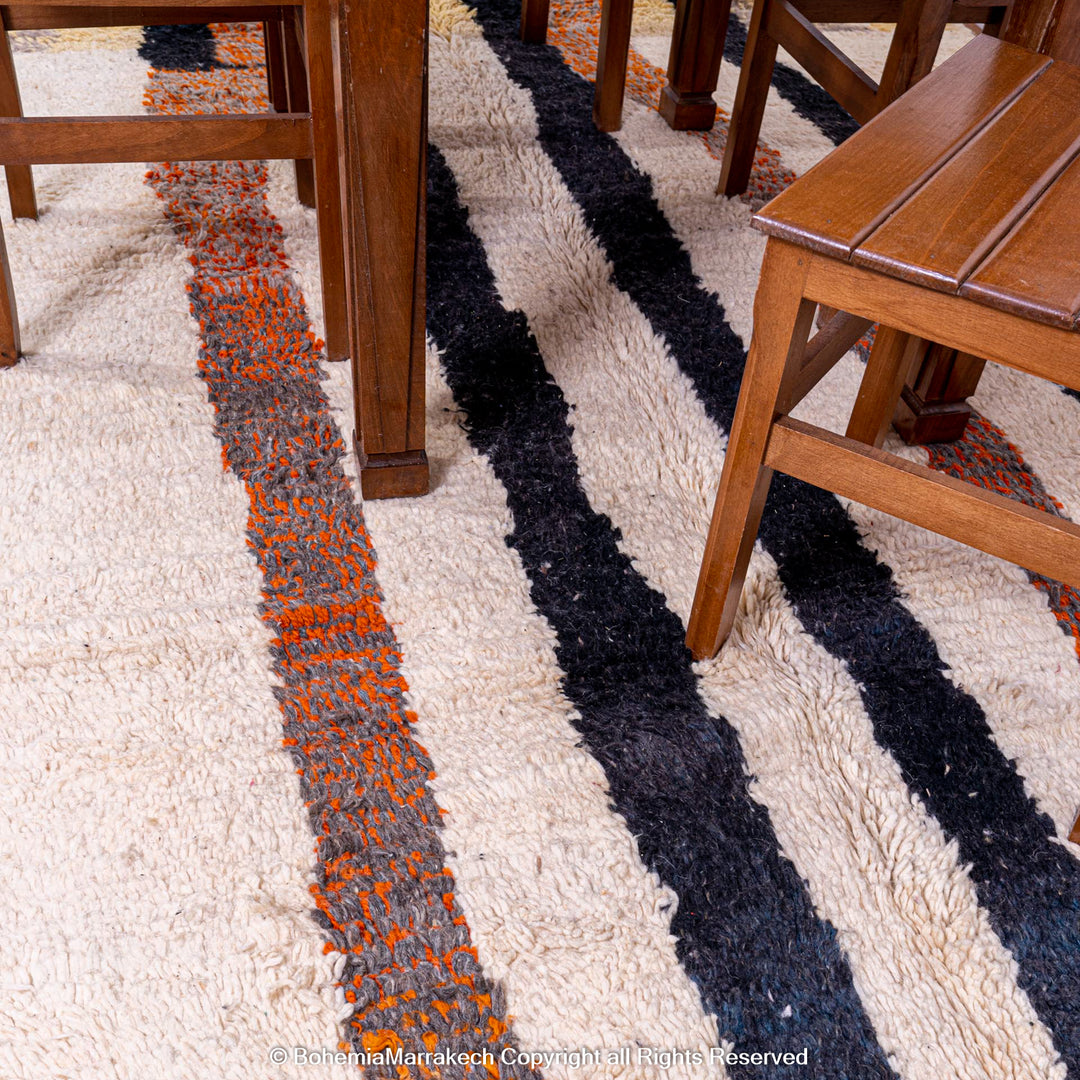 Striped Abstract Moroccan Rug under chairs, handmade from natural wool with black, orange, and earthy tones, featuring vertical stripes.