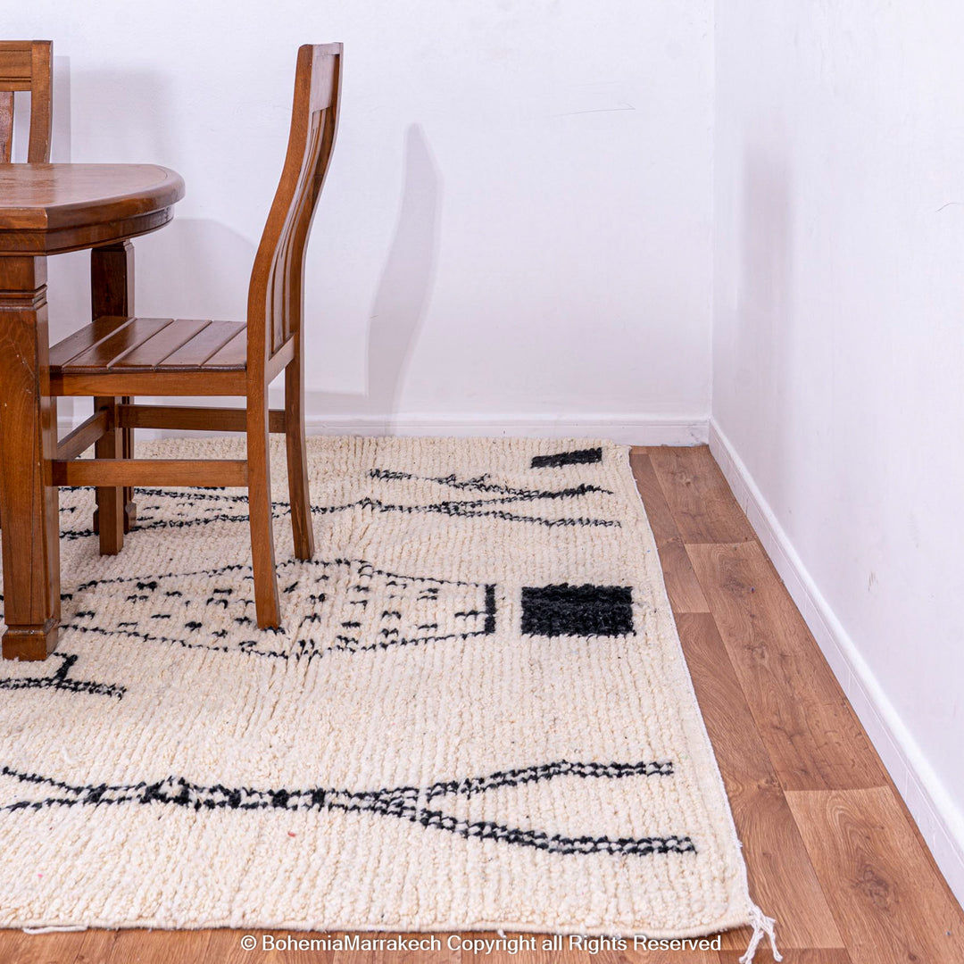 White Moroccan rug with black abstract diamond design under wooden dining set, handwoven from natural wool.