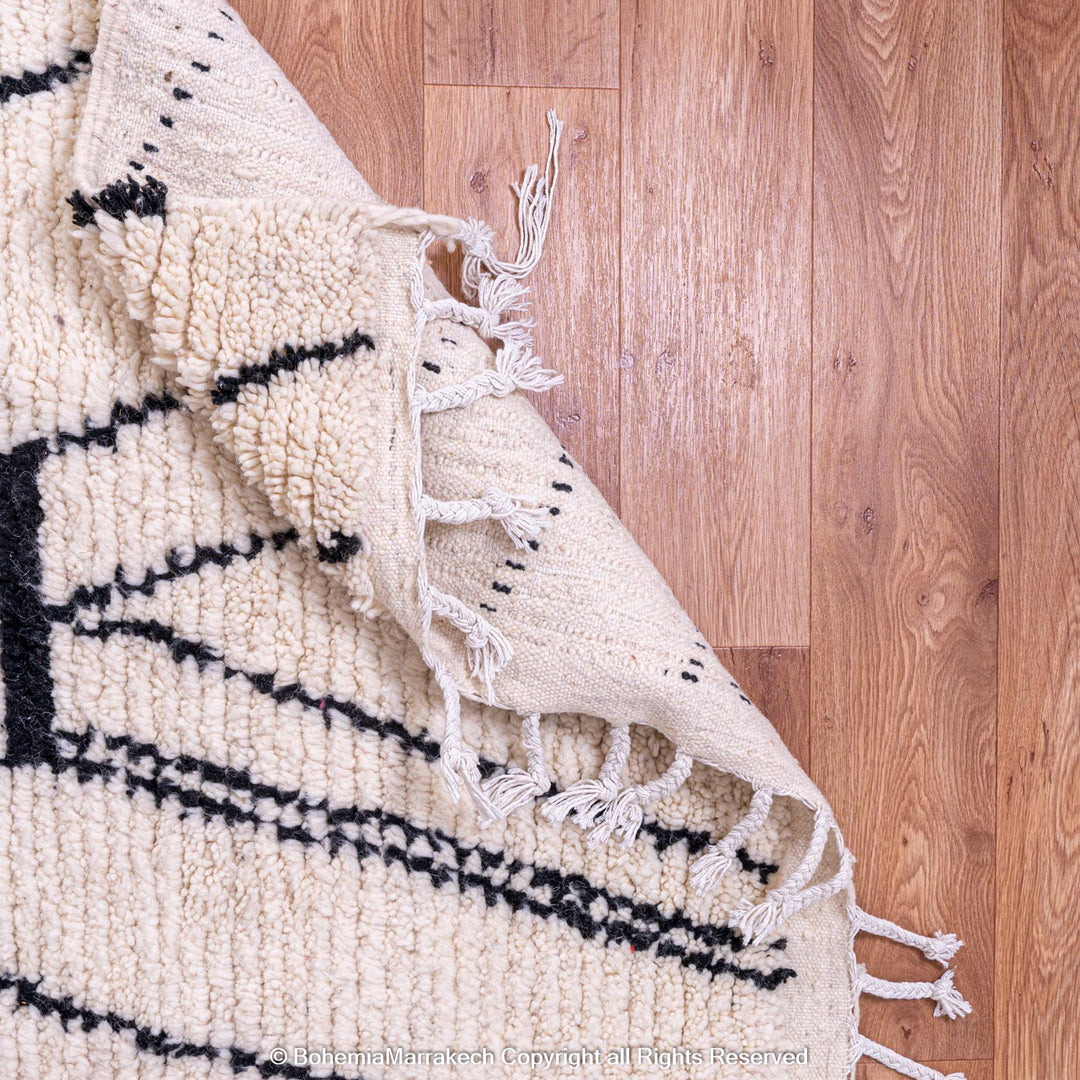 White Moroccan wool rug with abstract black diamond design, handwoven by Berber artisans, displayed on a wooden floor. Perfect for modern decor.